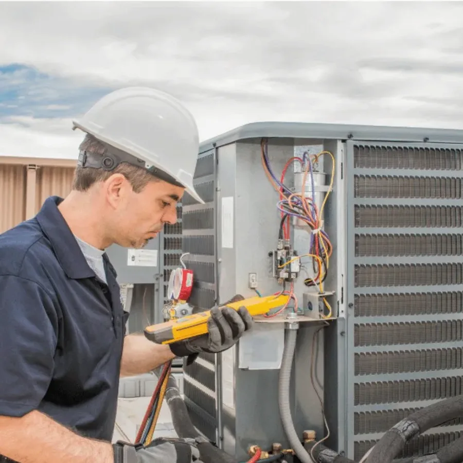 HVAC technician in a hard hat testing an outdoor air conditioner with a multimeter
